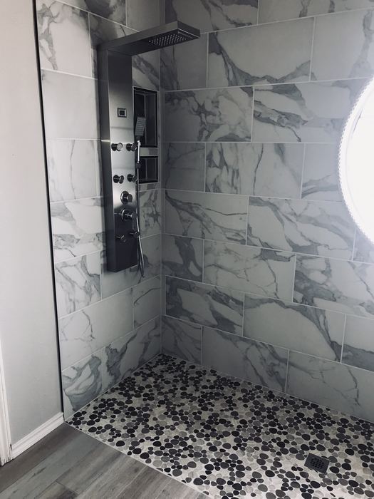 Remodeled walk-in shower with marble-look tile and pebble floor