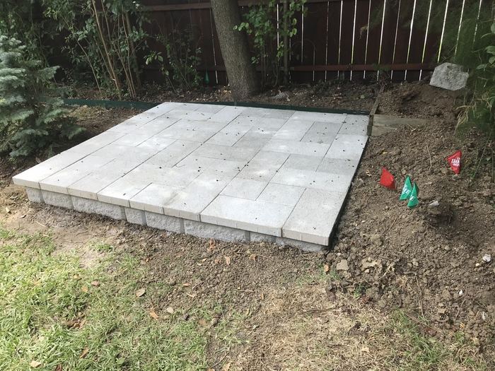 Level paver pad built on a block base in a backyard corner